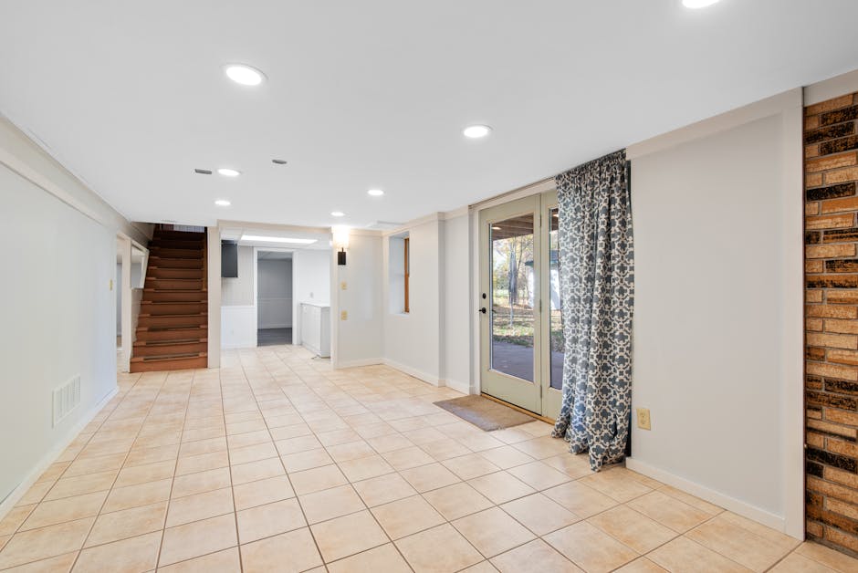 Bright and empty basement with tile flooring and glass doors leading outside.