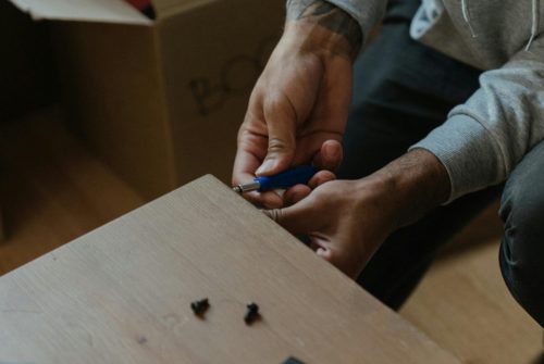 A man assembling a piece of furniture in a newly moved-in apartment setting.