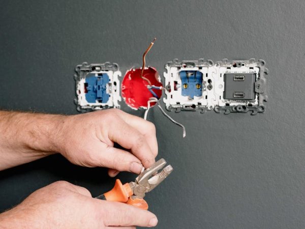 Crop faceless electrician using pliers for installation sockets and switches in new apartment